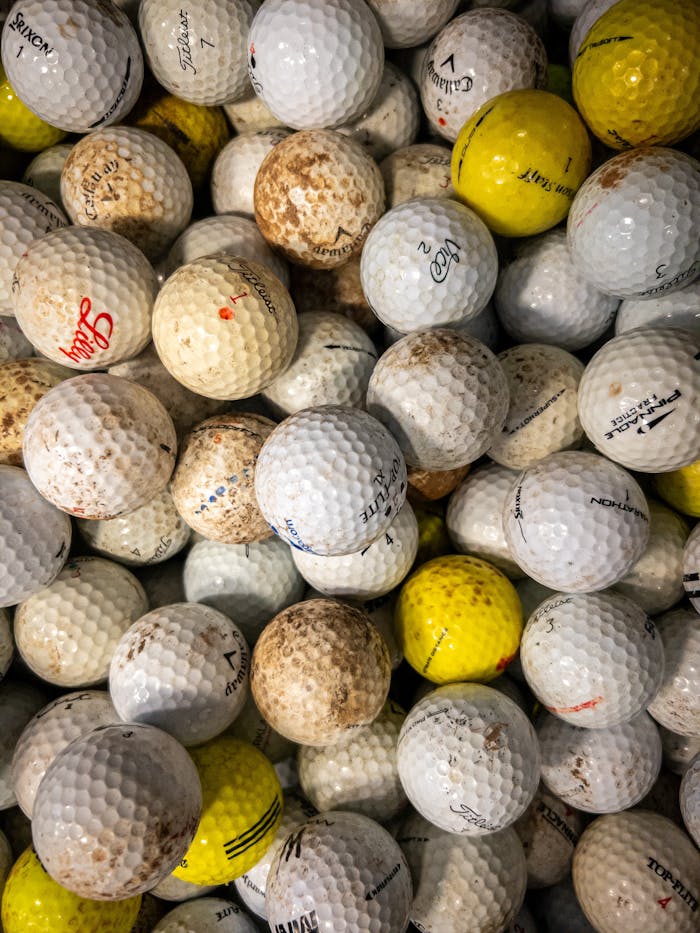 Close-up image of a heap of assorted used golf balls, showcasing diversity in color and brand.