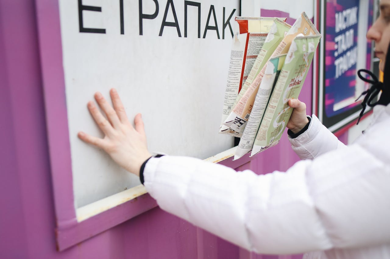 Person in white jacket recycles cartons at a purple recycling station, promoting eco-friendly habits.