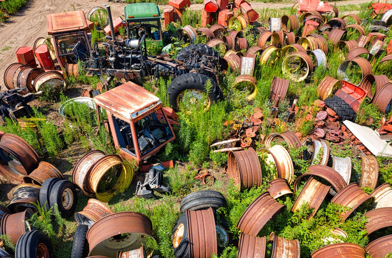 Aerial view of a junkyard with rusty tractor parts surrounded by grass and plants.